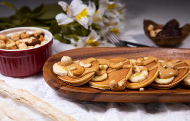 Pancakes with mix of nuts and peanut butter on white background with flowers. Trendy food.