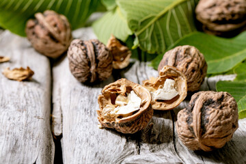 Fototapeta na wymiar Organic walnuts, whole and broken, with green leaves of walnut tree over old wooden background. Close up