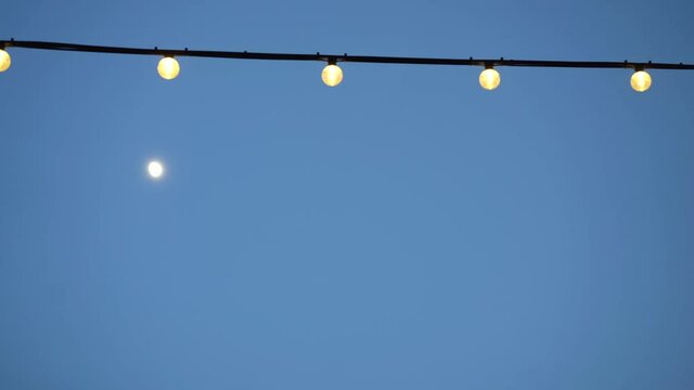 Low angle view of a moon and a string of lights at dawn