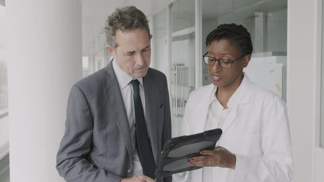 Doctors meeting in hospital corridor discussing test results on digital tablet computer technology