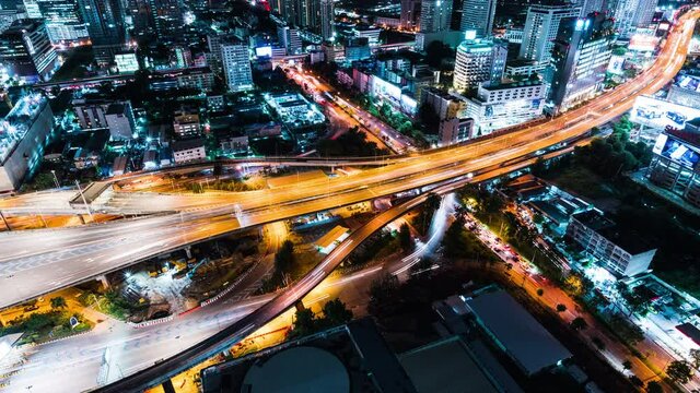 Time-lapse of car traffic transportation on highway road, toll gate at night. Cityscape view with construction crane on building. Urban transport lifestyle, Asian city life. High angle view, zoom out