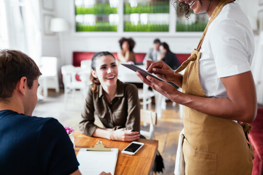 Crop waitress using tablet near couple
