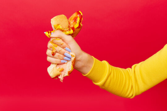 Woman's hand with painted blue nails squeezes hotdog