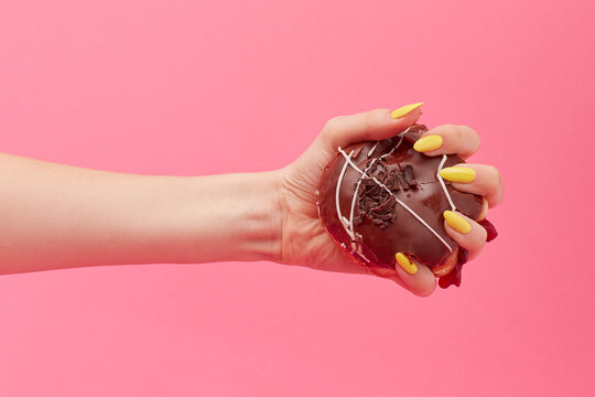 Woman with yellow nails squeezes a chocolate doughnut in her hand