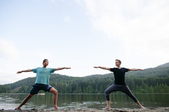 Two young men practicing yoga outside together in lake.