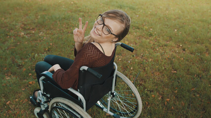 Beautiful disabled caucasian woman looking over the shoulder in the park, peace gesture. High...