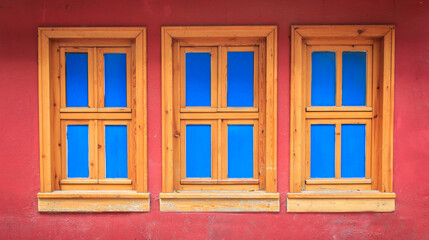 Three wooden windows on old red wall. Blue colors on windows. Historical house wall.