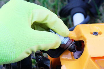 Defective spark plug on  background of grass trimmer,  hand in  glove holds