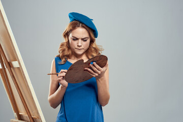 woman artist blue beret palette drawing on easel art creativity light background