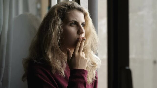 waiting, anxiety - worried young woman at window smoking a cigarette