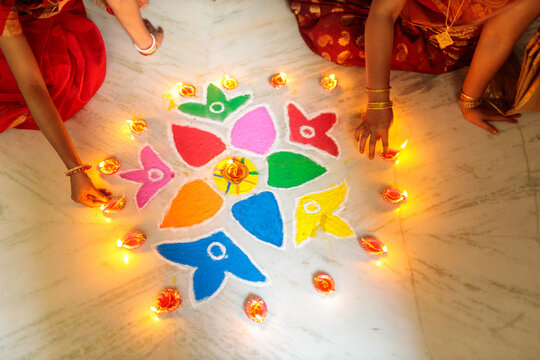 Indian women lighting oil lamps during diwali and decorating with rangoli