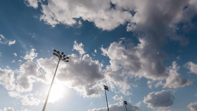 Timelapse with light towers of a football stadium against a sunset and summer clouds, cinematic fast and smooth movement of sky. Soccer stadium flashlights and evening time lapse.