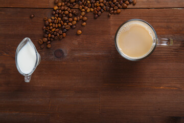 A mug of coffee with milk and a jug of cream on the table among the scattered coffee beans.