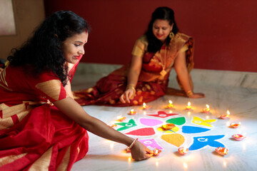 Indian women lighting oil lamps during diwali and decorating with rangoli