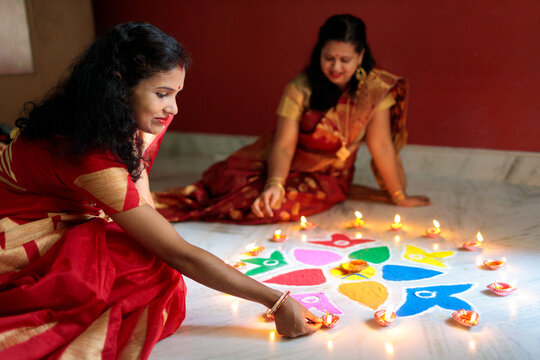 Indian women lighting oil lamps during diwali and decorating with rangoli
