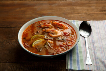 Tom yam soup with shrimp and lime in a light plate next to a spoon on a napkin.