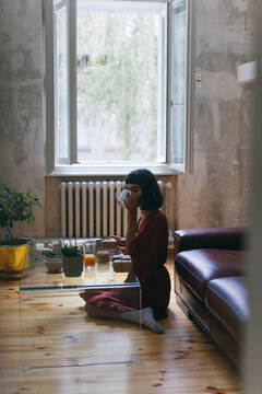 Woman sitting on a floor of a living room, drinking coffee
