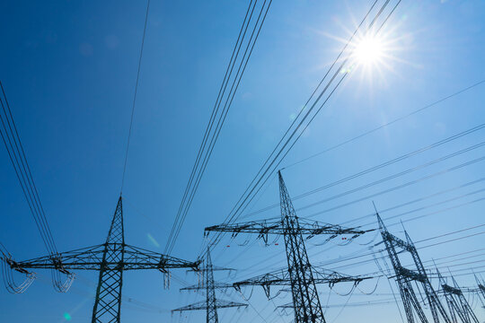 masts and power line for high voltage power supply in brillant backlit with sun flares