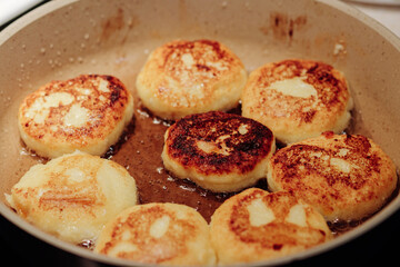 Cooking process of delicious fried syrniki close-up in the pan. Traditional in Ukraine, Belarus and Russia quark pancakes. Selective focus.
