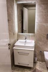 Modern bathroom indoor. White sink and mirror. Brown tiles on wall.