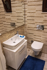 Modern bathroom indoor. White sink, mirror and white toilet. Brown tiles on wall.