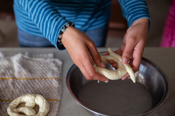 Closeup image of a pair of hands dipping raw pretzel dough into water in preparation for baking
