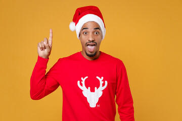 Excited young Santa african american man in red sweater Christmas hat hold index finger up with great new idea isolated on yellow background studio. Happy New Year celebration merry holiday concept.