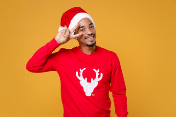 Smiling young Santa african american man in red sweater with deer Christmas hat showing victory sign isolated on yellow background studio portrait. Happy New Year celebration merry holiday concept.