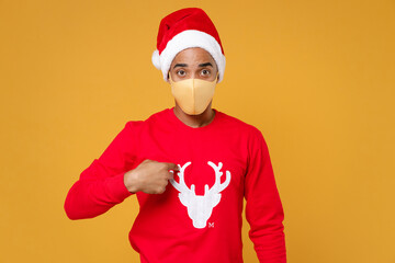 Fototapeta na wymiar Young Santa african american man in Christmas hat face mask safe from coronavirus virus covid-19 point index finger on himself isolated on yellow background Happy New Year celebration holiday concept.