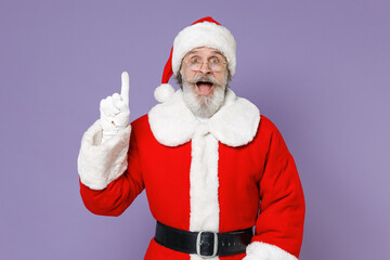 Fototapeta na wymiar Santa Claus man in Christmas hat red suit coat white gloves glasses holding index finger up with great new idea isolated on violet background studio. Happy New Year celebration merry holiday concept.
