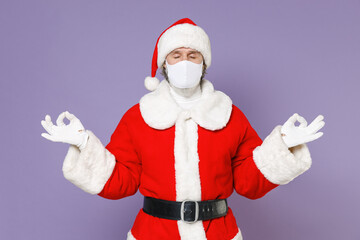 Fototapeta na wymiar Santa Claus man in Christmas hat red coat face mask to safe from coronavirus virus covid-19 hold hands in yoga gesture isolated on violet background. Happy New Year celebration merry holiday concept.