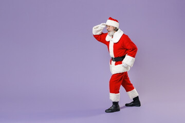 Full length side view portrait worried Santa Claus man in Christmas hat suit hold hand at forehead looking far away distance isolated on violet background. Happy New Year celebration holiday concept.