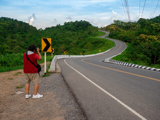 man taking picture at three shaped curve road on green mountain forest