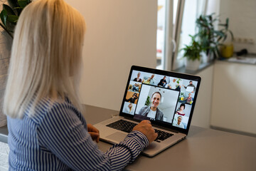 Fototapeta na wymiar Back view of business woman talking to her colleagues about plan in video conference. Multiethnic business team using laptop for a online meeting in video call. Group of people smart working from home