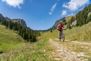 Naklejka premium nice senior woman riding her electric mountain bike up to the Schreiber Sattel below Winterstaude summit in the Bregenzer Wald mountain range in Vorarlberg, Austria