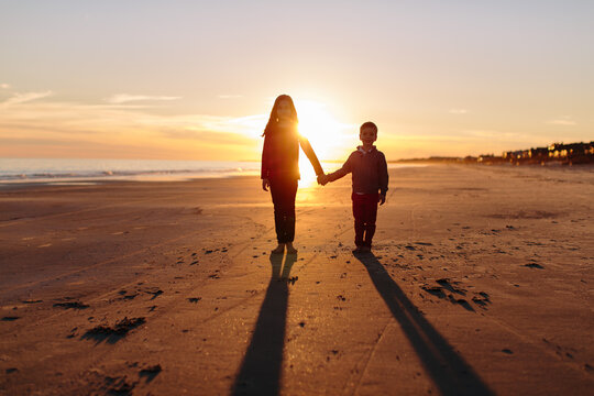 Brother and sister holding hands with sun setting behind them