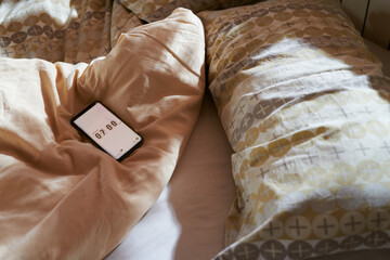 Smartphone with alarm clock on bed