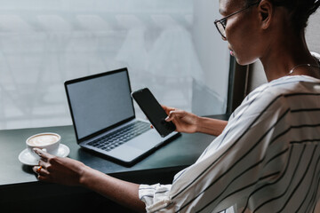 Charming smiling woman browsing smartphone at table in cafe at morning light