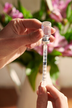 Crop lady preparing hormonal medicine for injection near flowers