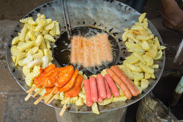 Chinese street food: deep fried sausages, chicken and potatoes, in a traditional frying equipment....