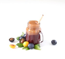 Smoothies combined from black and yellow plums in a glass jar with bamboo straw on a white...
