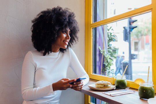Smiling young woman using mobile phone in cafe