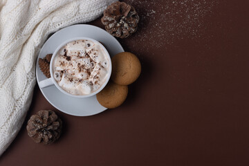 Autumn and winter concept. Top view of cup of cocoa with marshmallows, cookies, white sweater, pine cones and snow on brown background.  Chestnut color. Hygge