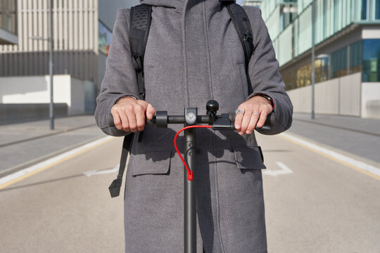 Man holding handlebars of electric scooter on empty road in city