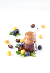 Smoothies combined from black and yellow plums in a glass jar with bamboo straw on a light background