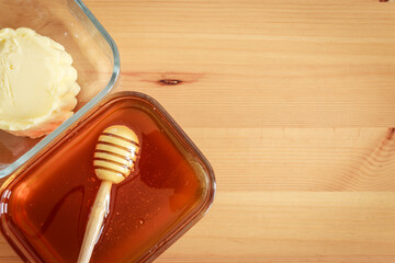 Honey in glass jar with wooden spoon and butter in glass jar on wooden table with copy space