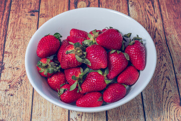 Strawberries in a white bowl on a wooden table in a rustic setting