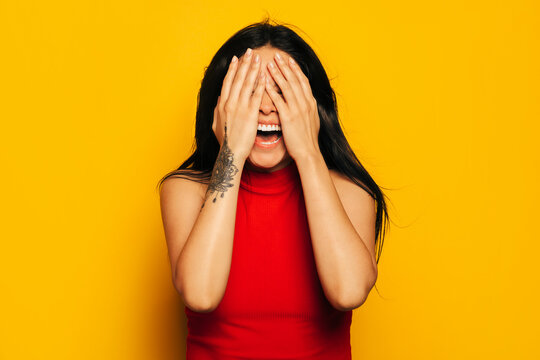 Gorgeous mixed race woman smiling over yellow background and covering face with hands