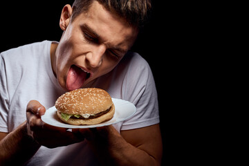 Man with hamburger plates on black background in white t-shirt portrait cropped view of fast food