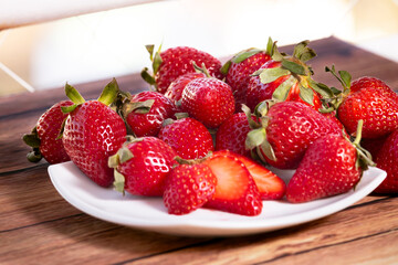 Strawberries on a white square plate on a wooden table in a rustic setting